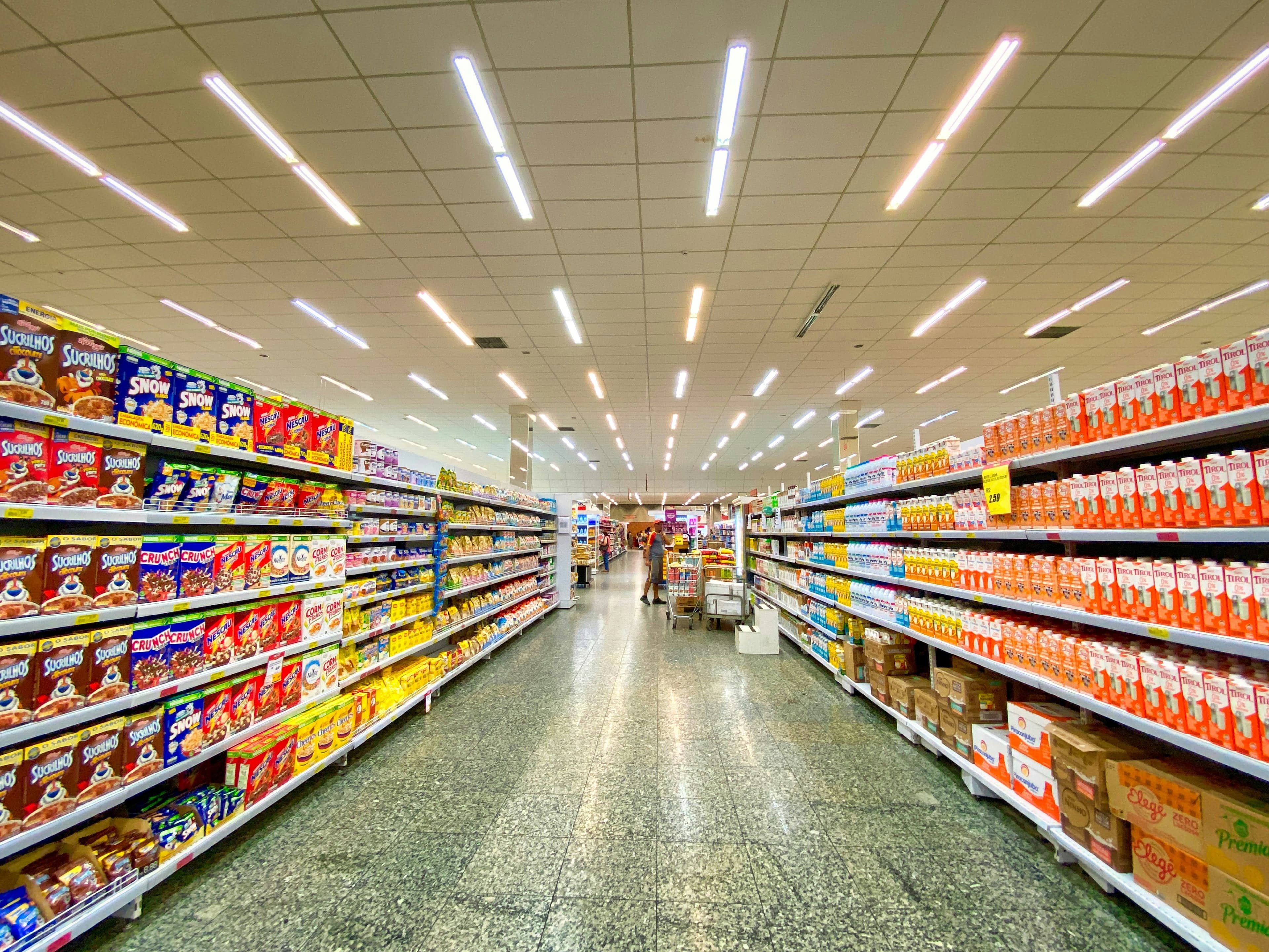 A grocery store aisle with shelves stocked with cereal boxes and milk cartons