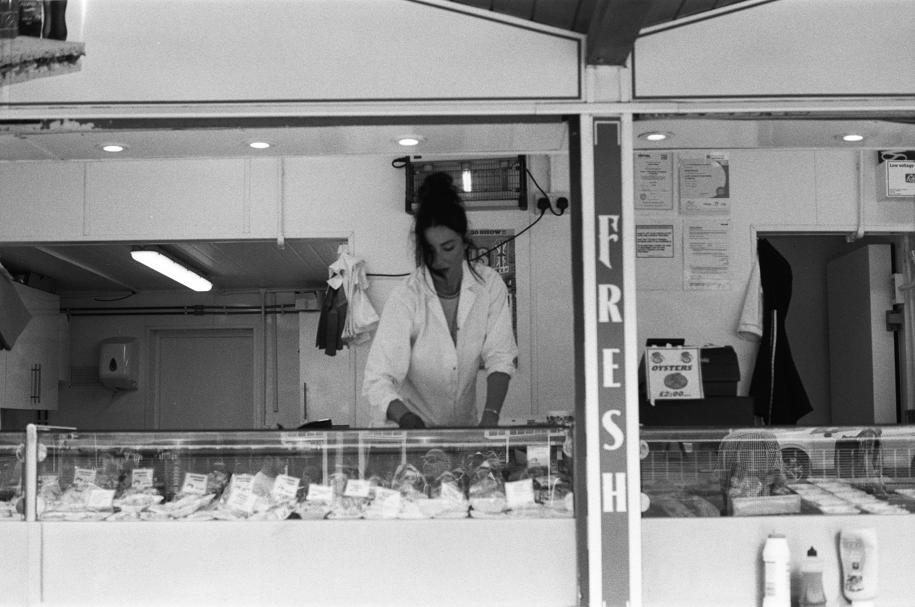 grayscale photo of woman in white coat standing in front of glass window
