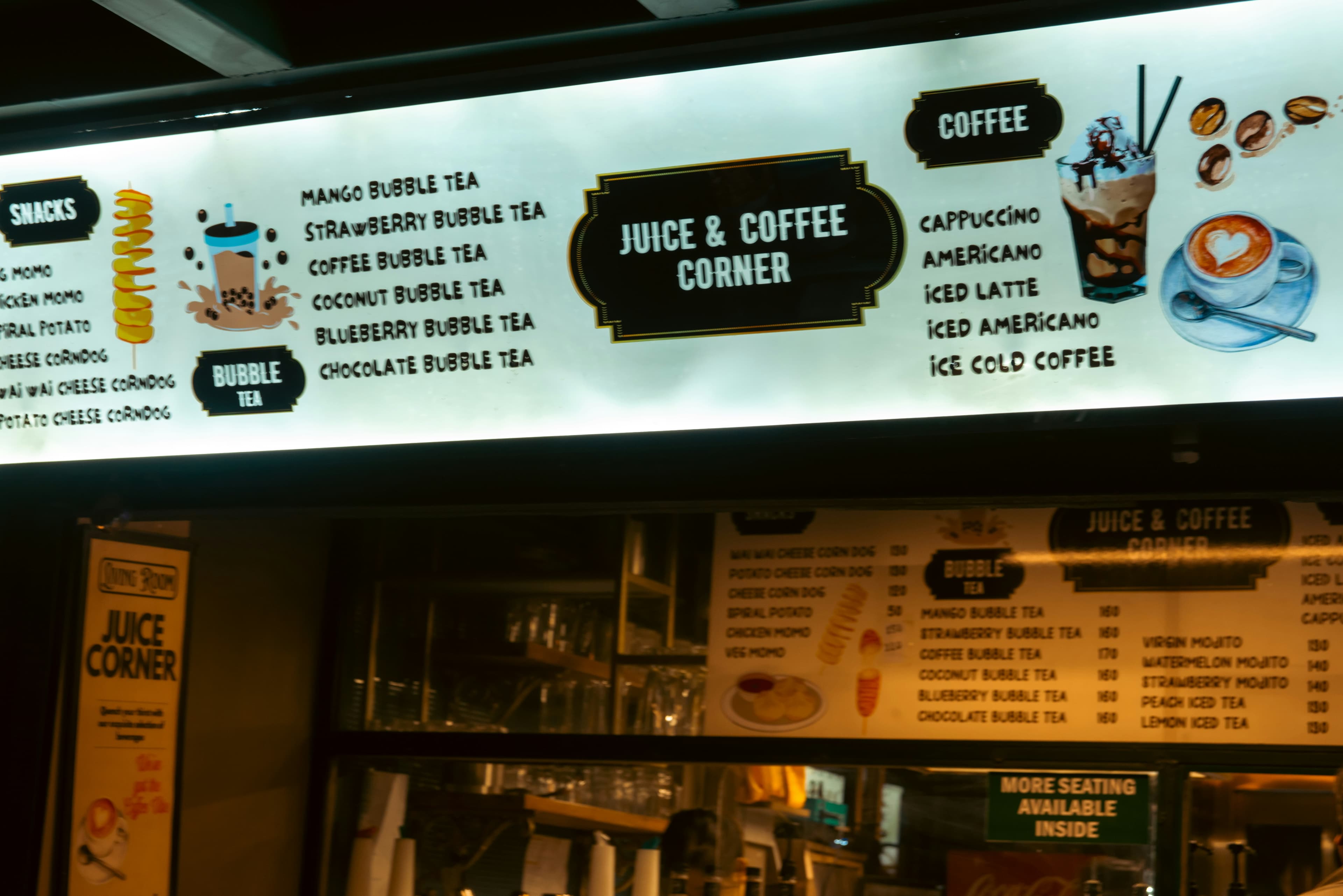 A glowing menu board at a “Juice & Coffee Corner” displaying a variety of drinks and snacks, including bubble tea, corndogs, and iced coffee. The illuminated signage captures the inviting evening atmosphere of a local café in Delhi’s Majnu ka Tila market.