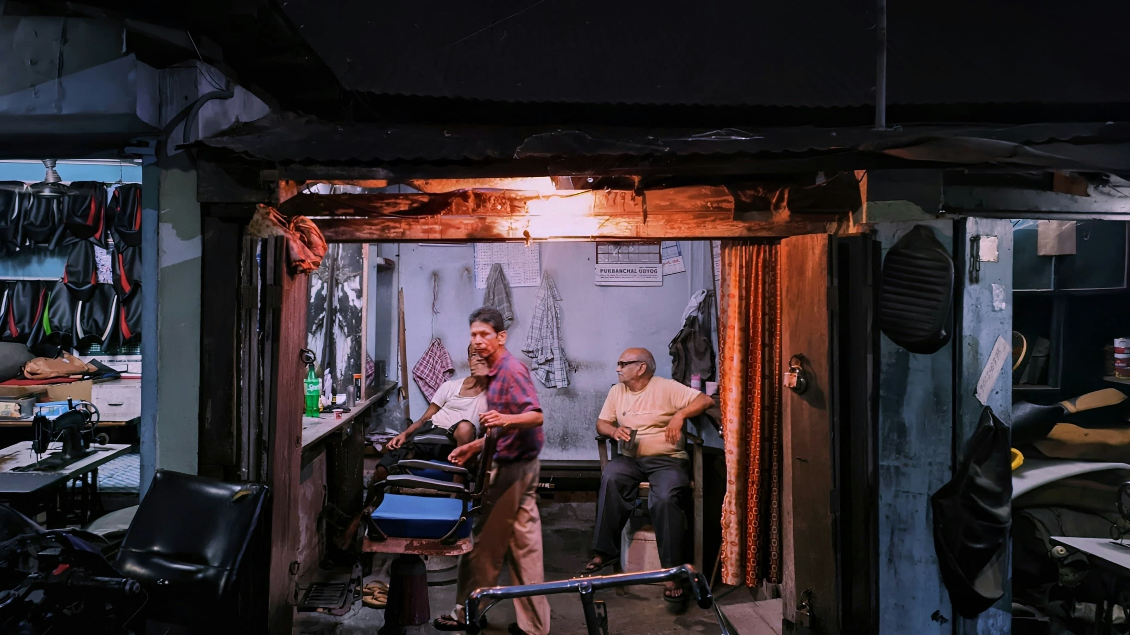 Two men in a dimly lit barbershop with a single warm overhead light